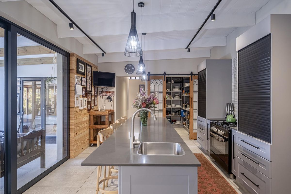 Modern kitchen featuring a large central island with a stainless steel sink, sleek cabinetry, built-in gas stove, and a convenient walk-in pantry with sliding doors.