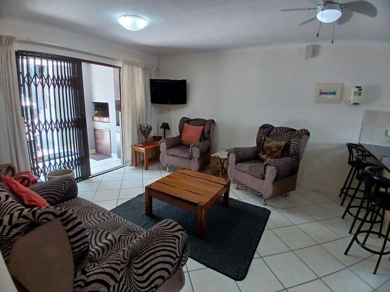 Open plan living area featuring ceramic floor tiles, a breakfast bar, and a sliding door leading to a patio with a built-in braai.
