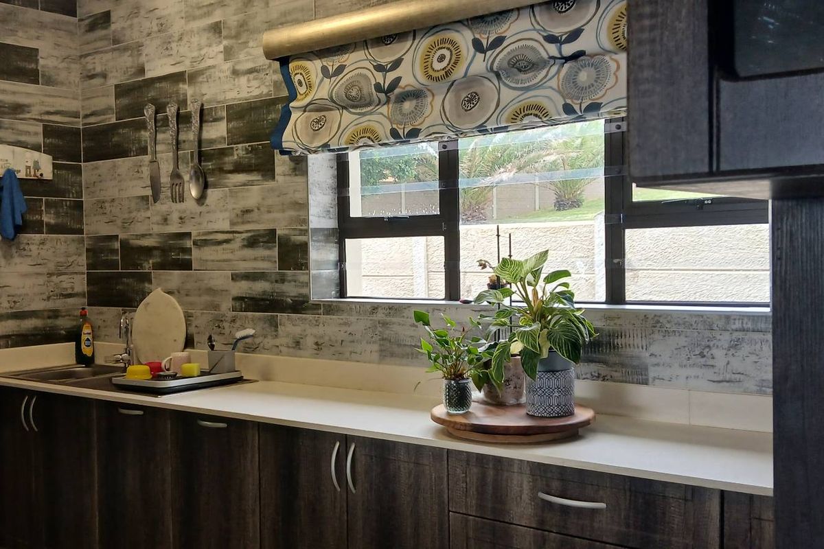 A functional kitchen area featuring dark wood-look cabinetry, a light-toned countertop, and a distinctive textured tiled splashback with a window view.