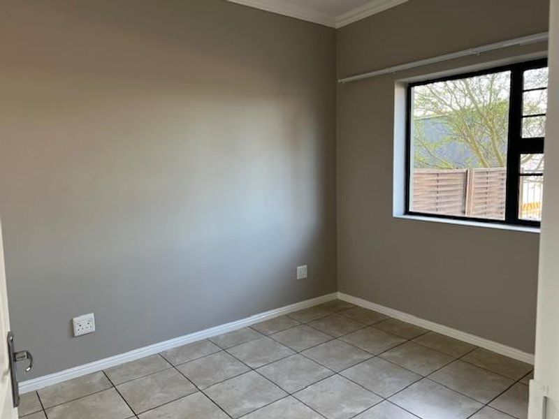 A clean, empty bedroom featuring neutral wall paint, tiled flooring, and a large black-framed window providing natural light.