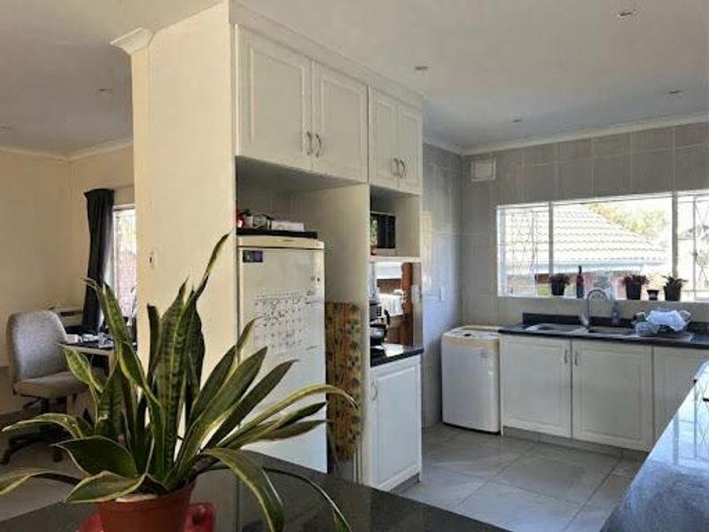 A functional kitchen featuring white cabinetry, granite countertops, a double sink, and tiled backsplash with ample natural light from the window.