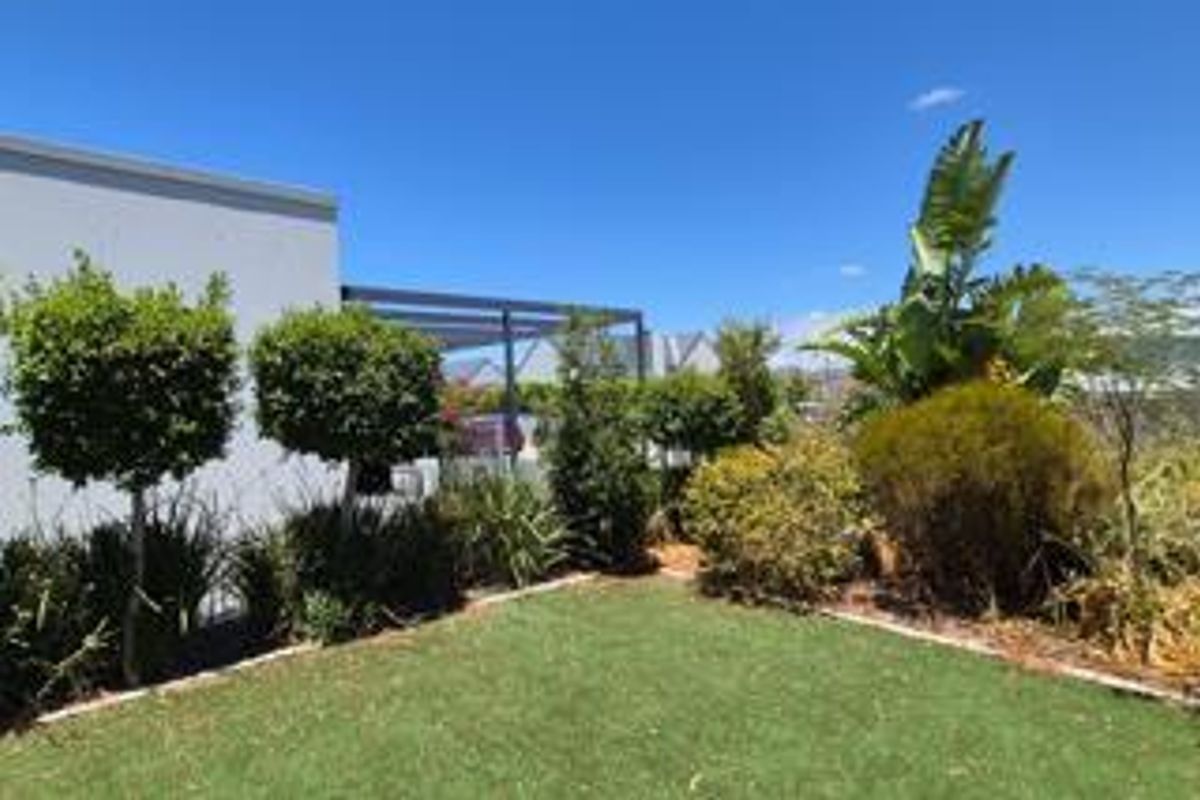 A well-maintained rear garden area featuring a manicured lawn, established shrubs, and a covered patio structure attached to the main dwelling.