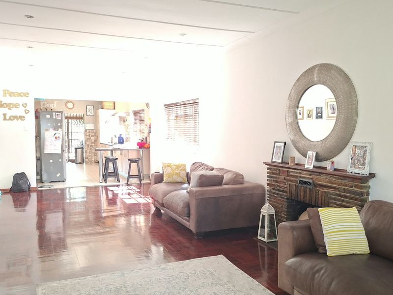 Spacious open-plan living area featuring polished wooden floors, a stone fireplace, and a connected kitchen with a breakfast island.