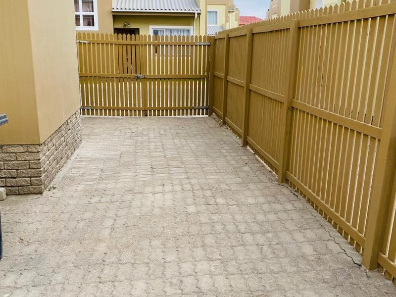 A private rear courtyard area featuring paved flooring, enclosed by a timber picket fence and gate, with stone cladding detail on the building exterior.