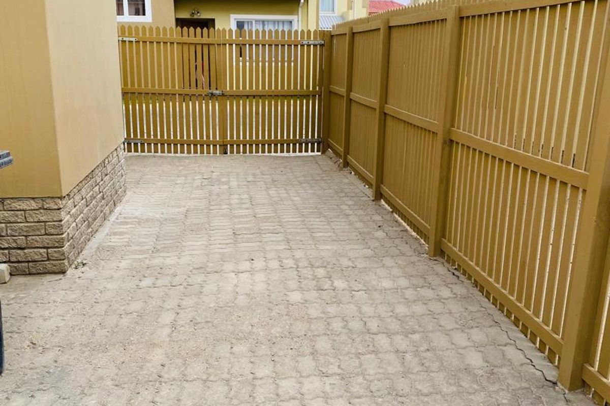 A private rear courtyard area featuring paved flooring, enclosed by a timber picket fence and gate, with stone cladding detail on the building exterior.