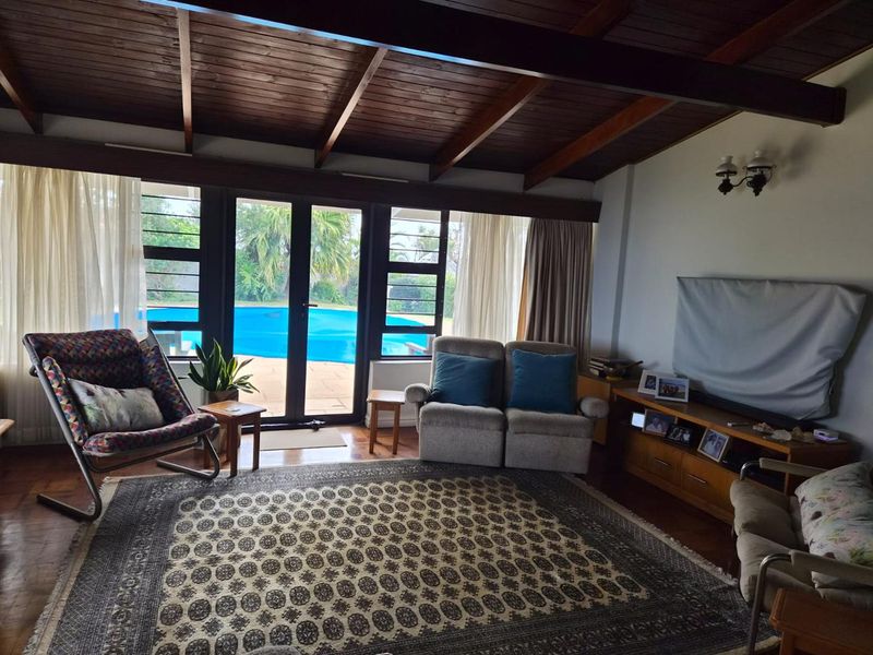 Spacious living room featuring exposed timber beam ceilings, hardwood flooring, and large glass doors providing direct access to the outdoor pool area.
