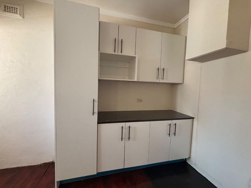 A compact kitchen area featuring white built-in cabinetry, dark countertops, and an extractor fan housing, presenting a clean, functional space ready for updates.