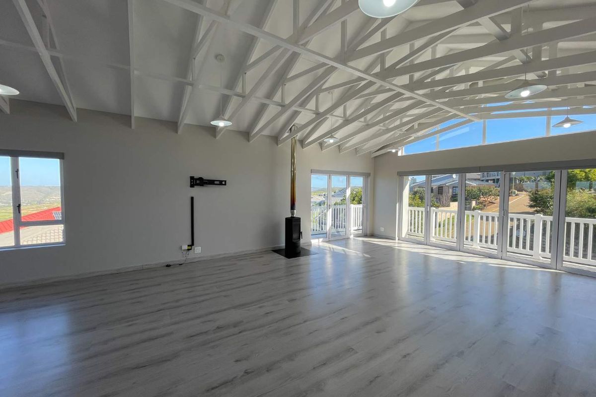 Spacious open-plan living area featuring high exposed white trusses, modern laminate flooring, a freestanding fireplace, and large sliding doors leading to a balcony.