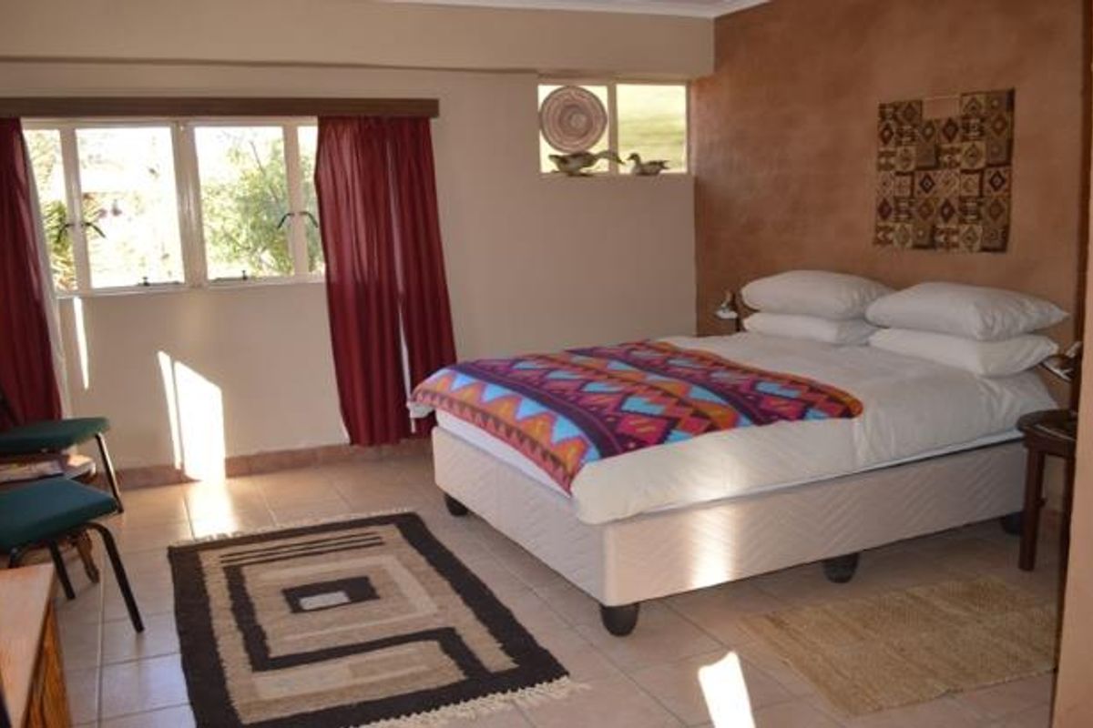 A bedroom featuring tiled flooring, neutral walls with a textured accent wall, and natural light through large windows.