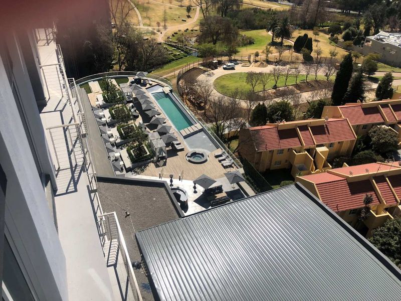 An elevated aerial view of the apartment complex pool area, featuring a lap pool, jacuzzi, and landscaped outdoor deck space.