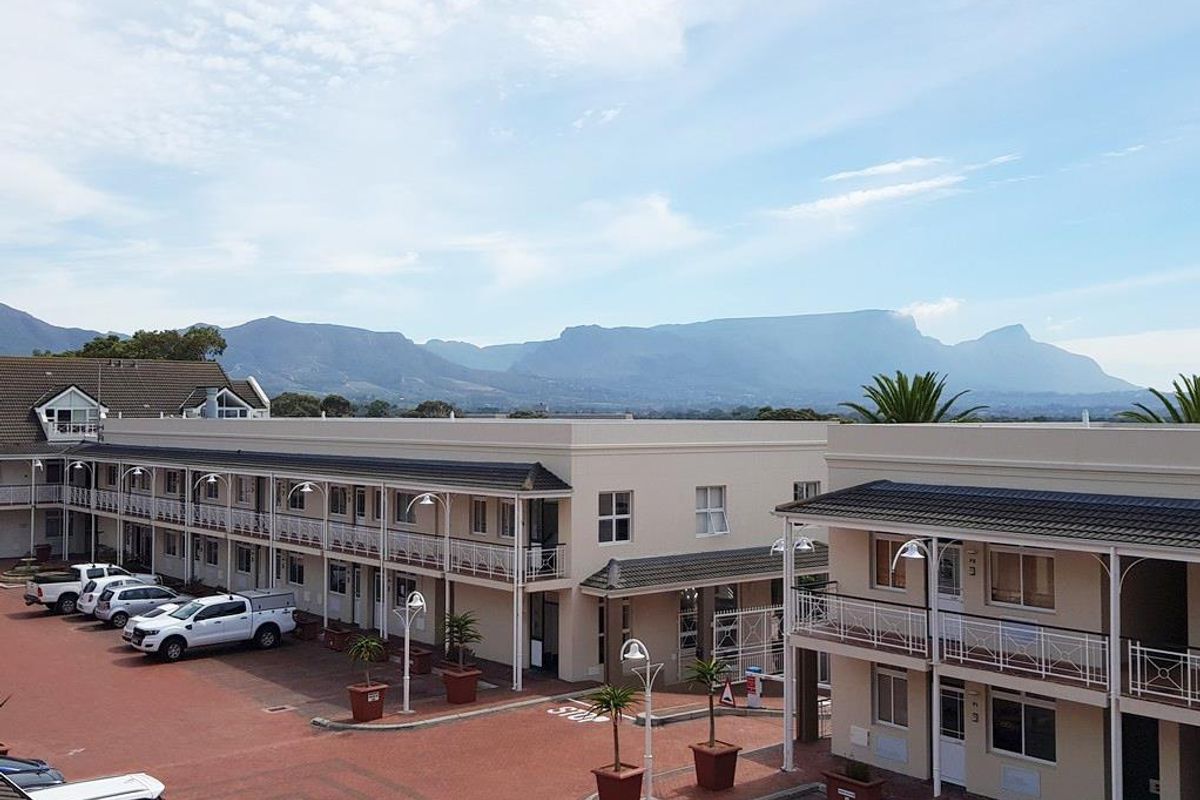 Elevated view of a multi-story office complex featuring paved parking areas, covered walkways, and scenic mountain views in the background.