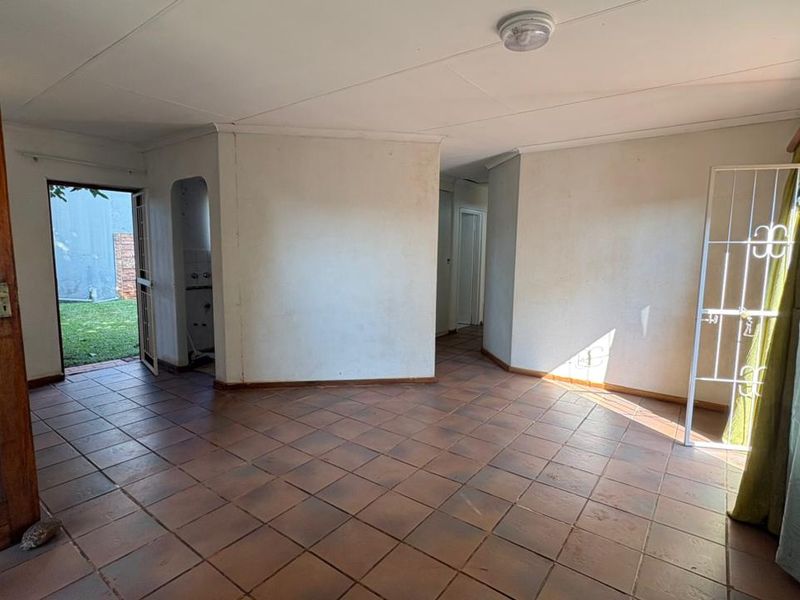 An empty living room featuring tiled flooring, an archway leading to a secondary space, and direct access to the exterior through a security gate.