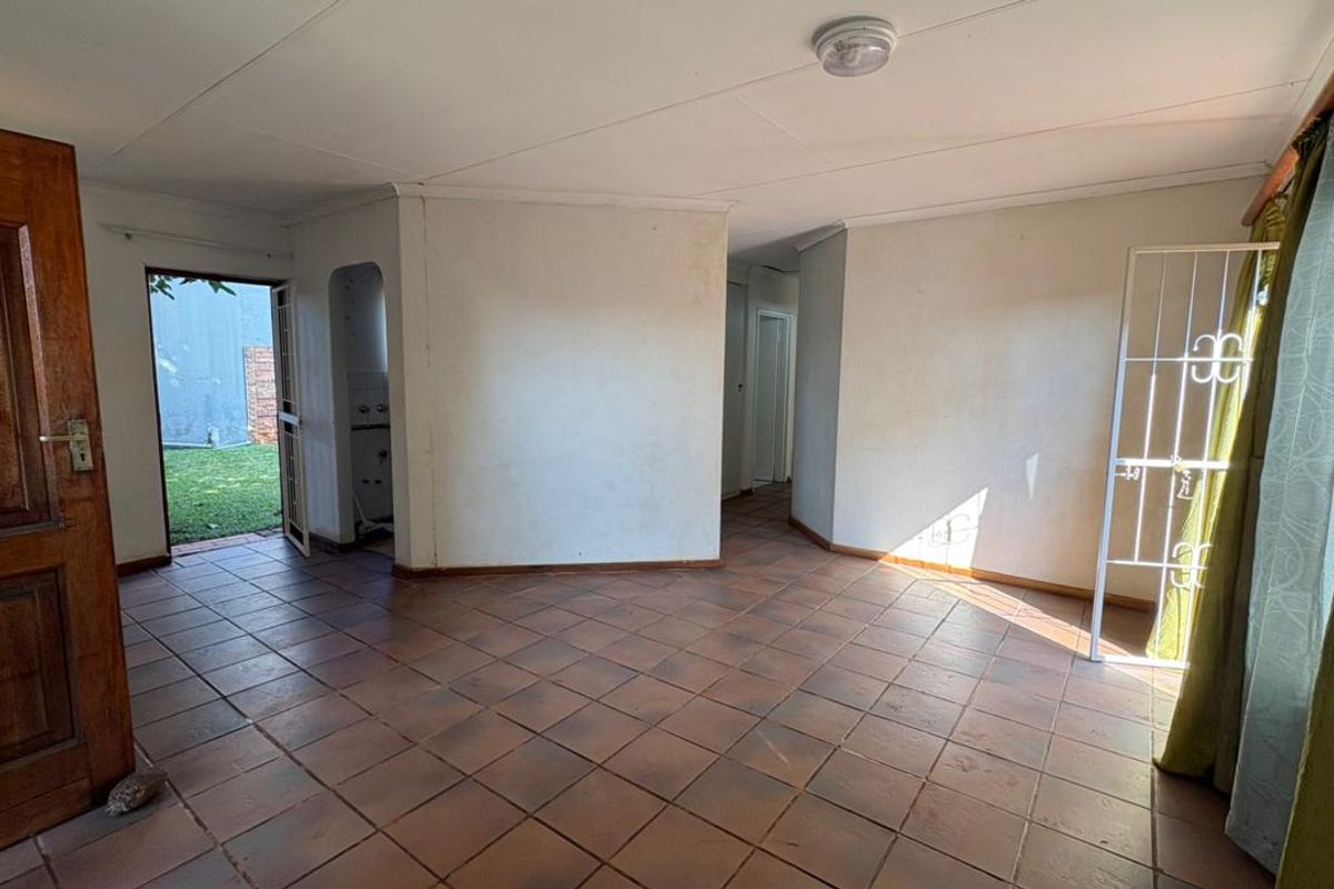 An empty living room featuring tiled flooring, an archway leading to a secondary space, and direct access to the exterior through a security gate.