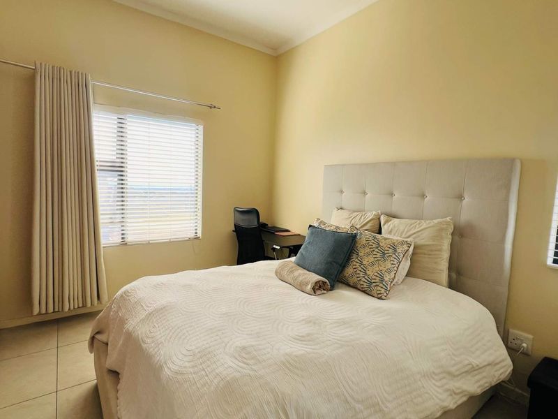 A well-lit bedroom featuring tiled flooring, built-in wardrobe storage, and dual windows with venetian blinds, offering a functional and comfortable living space.