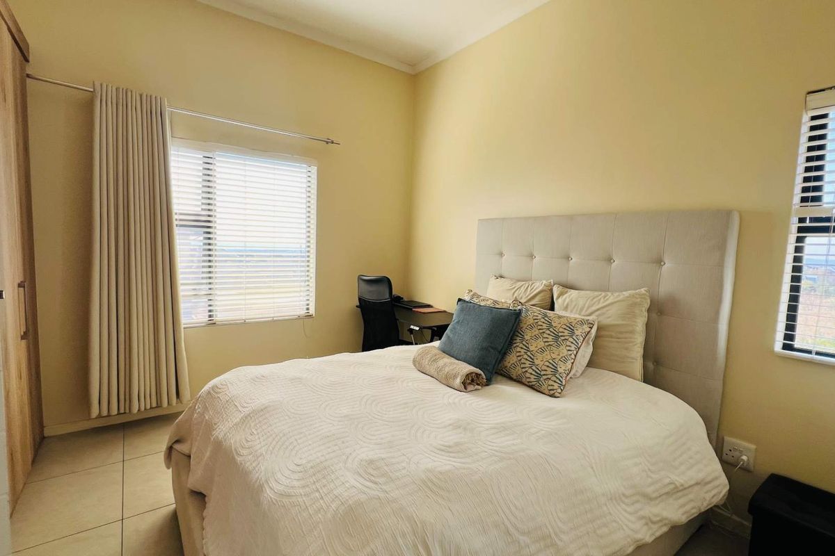 A well-lit bedroom featuring tiled flooring, built-in wardrobe storage, and dual windows with venetian blinds, offering a functional and comfortable living space.