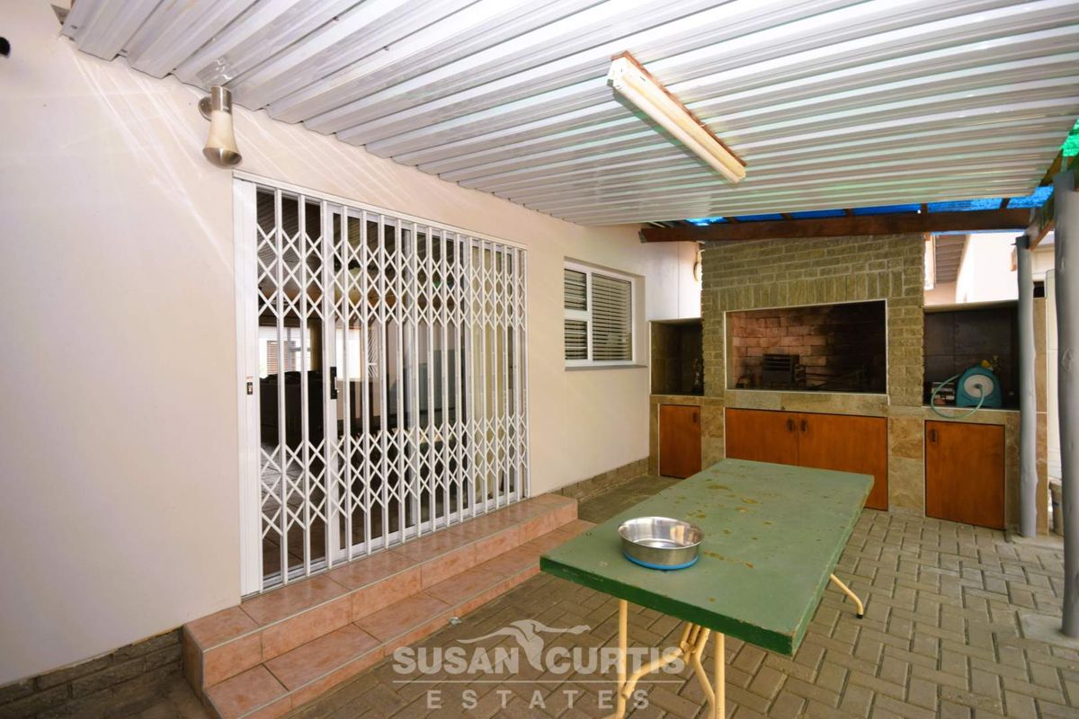 Covered outdoor patio area featuring a built-in braai, paved flooring, and secure sliding door access to the main living space.