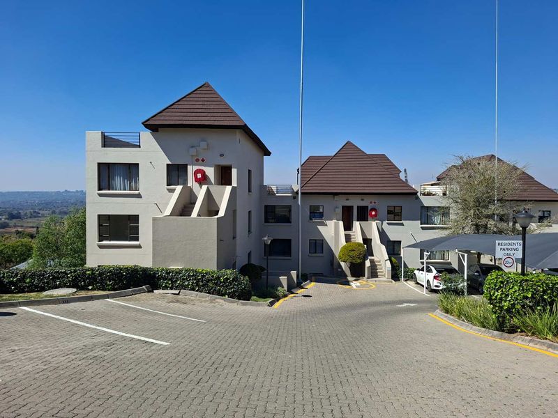 Exterior view of an apartment complex featuring a paved driveway, resident parking carports, and multi-level residential units with tiled roofing.