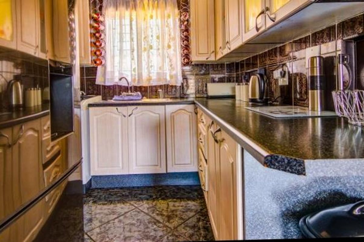 A compact kitchen featuring traditional laminate cabinetry, dark tiled backsplash, built-in oven, and durable tiled flooring, offering a functional layout for meal preparation.
