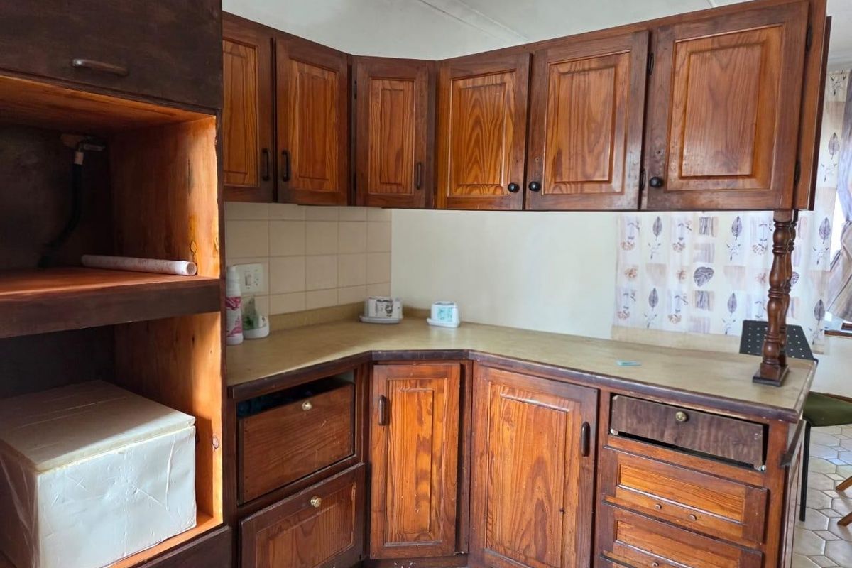 A dated kitchen featuring traditional wooden cabinetry, laminate countertops, and tiled flooring, offering significant potential for a modern renovation.