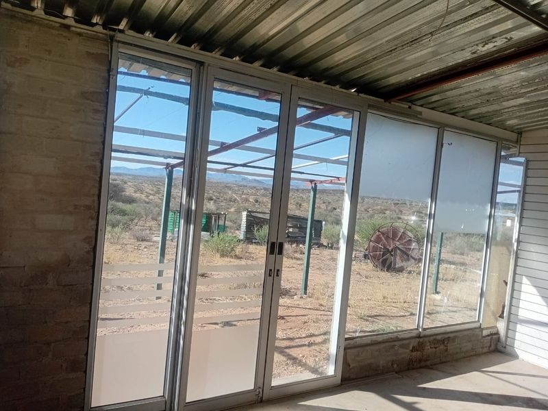 A semi-enclosed patio area featuring aluminium sliding doors, a corrugated metal roof, and views over the surrounding agricultural land.