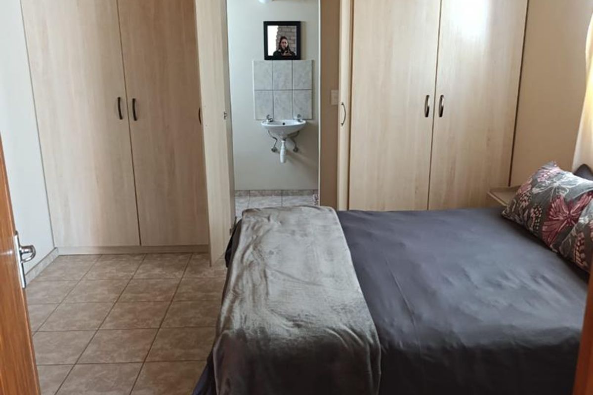 Bedroom featuring a vaulted timber ceiling, tiled flooring, and built-in wardrobes, with an adjoining en-suite bathroom visible through the doorway.