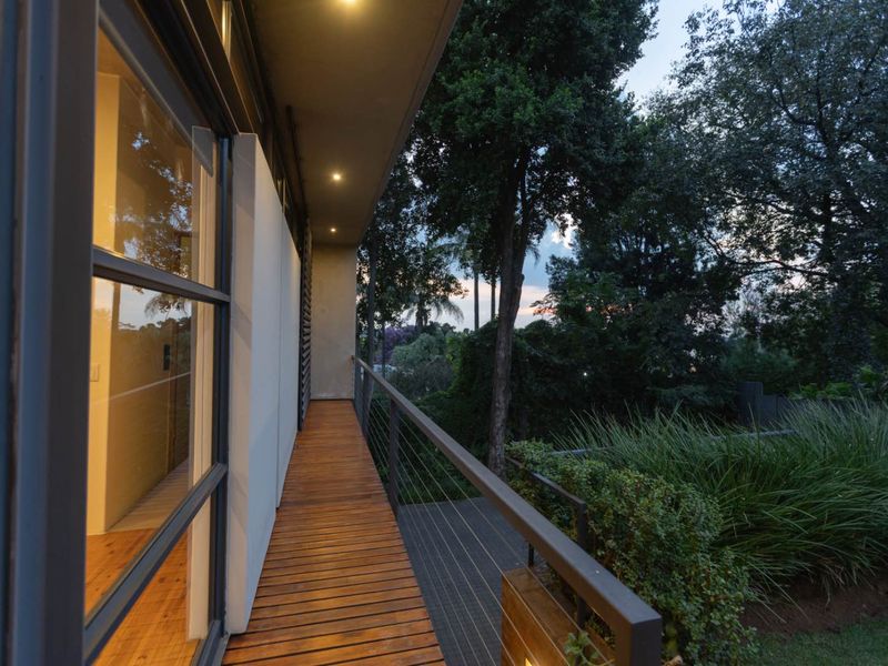 A modern, elevated balcony featuring timber decking, a sleek metal balustrade, and recessed lighting, overlooking a lush garden area.