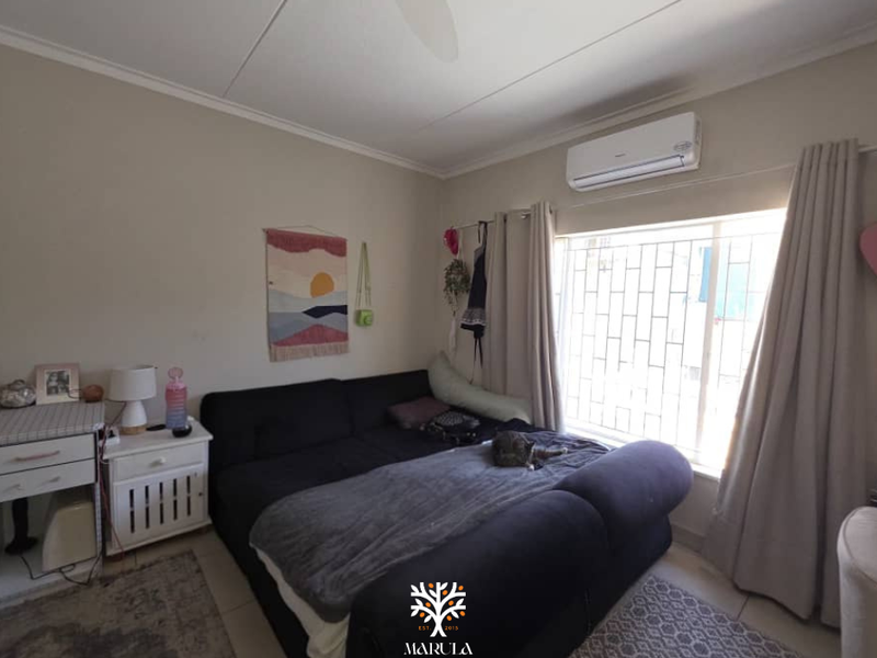A bedroom featuring tiled flooring, a wall-mounted split-system air conditioner, and a window fitted with security bars.