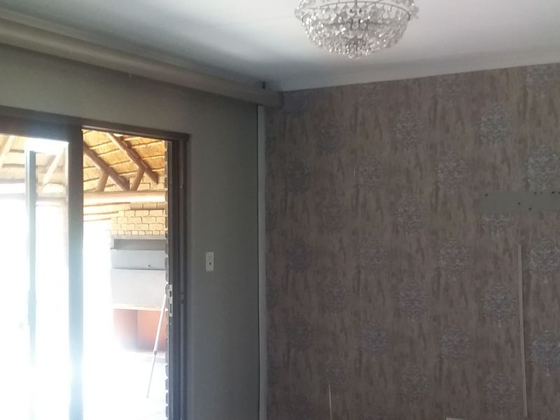 An empty living room featuring a crystal chandelier, patterned wallpaper, and a sliding glass door providing access to an outdoor patio area.
