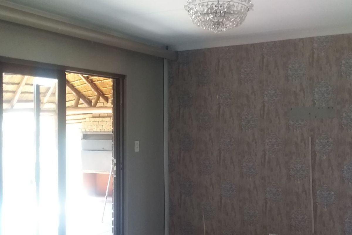 An empty living room featuring a crystal chandelier, patterned wallpaper, and a sliding glass door providing access to an outdoor patio area.