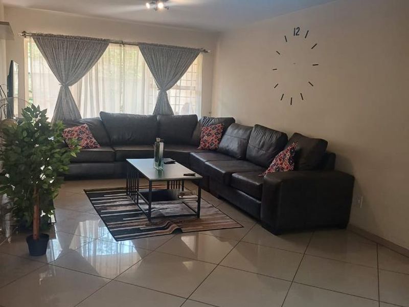 A spacious living room featuring polished tiled flooring, modern track lighting, and large windows with installed curtain rails.
