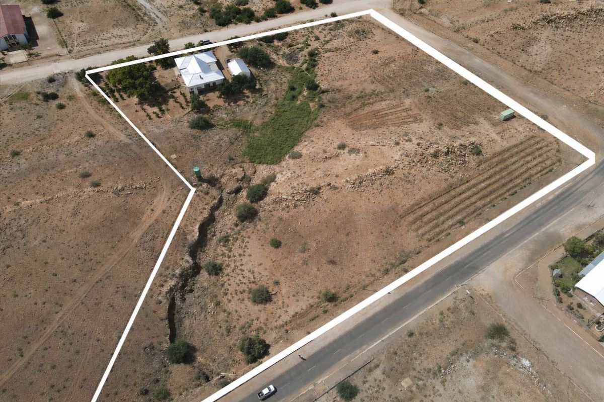 Aerial view of a large, expansive plot of land featuring a residential dwelling, natural terrain, and clear boundary markings.
