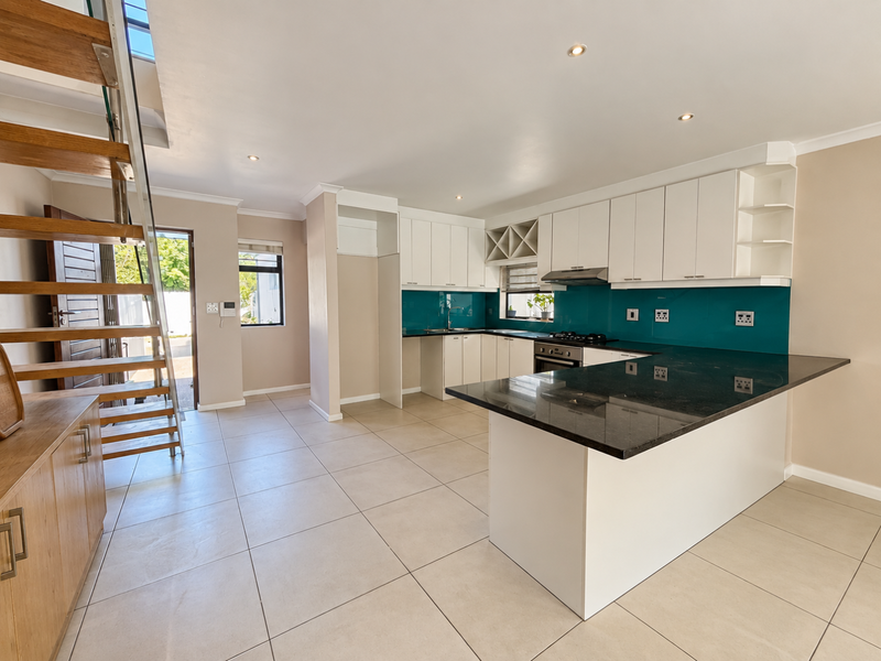 Modern open-plan kitchen featuring white cabinetry, a dark stone island, and a vibrant teal splashback, seamlessly integrated with a contemporary staircase.