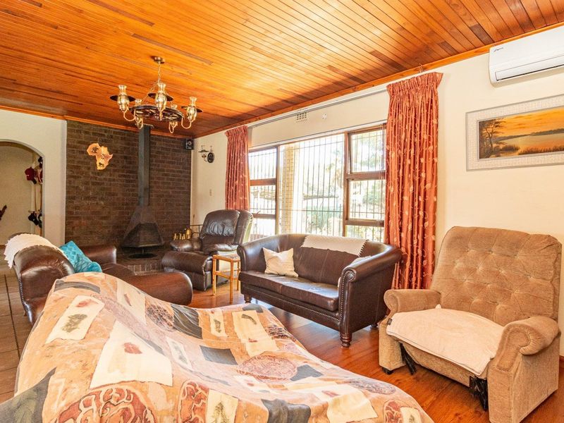 A cozy living room featuring a wood-paneled ceiling, a brick fireplace with a freestanding unit, and timber flooring, equipped with a wall-mounted air conditioner.