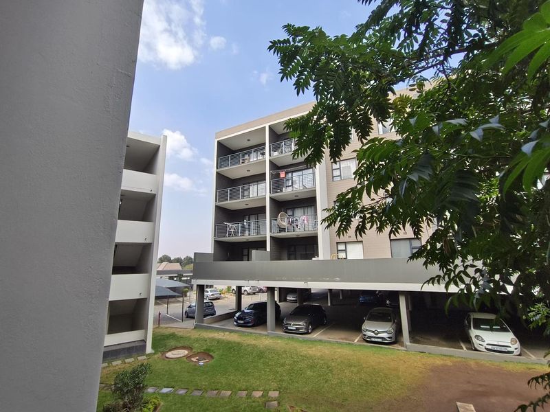 Exterior view of a modern apartment complex featuring multi-level balconies, covered ground-floor parking, and a landscaped garden area.
