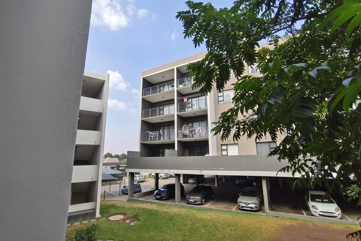 Exterior view of a modern apartment complex featuring multi-level balconies, covered ground-floor parking, and a landscaped garden area.