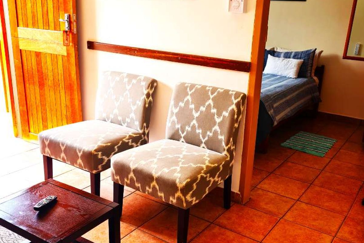 A view of a living area with terracotta floor tiles and a wooden door, leading into an adjacent bedroom space.