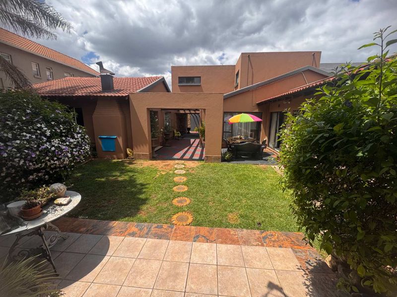 Rear view of the property featuring a tiled patio, covered outdoor entertainment area, and a landscaped garden with a lawn.
