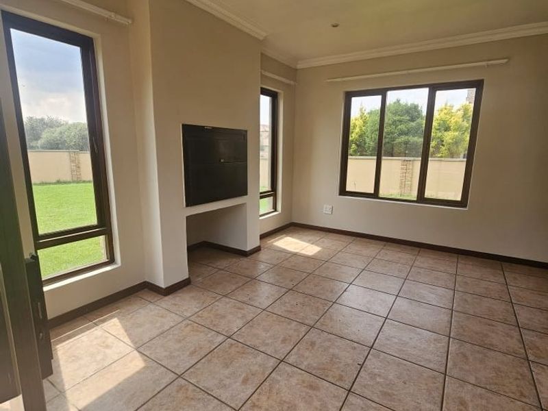 A bright, empty living room featuring tiled flooring, a built-in fireplace, and large windows providing natural light and views of the garden.