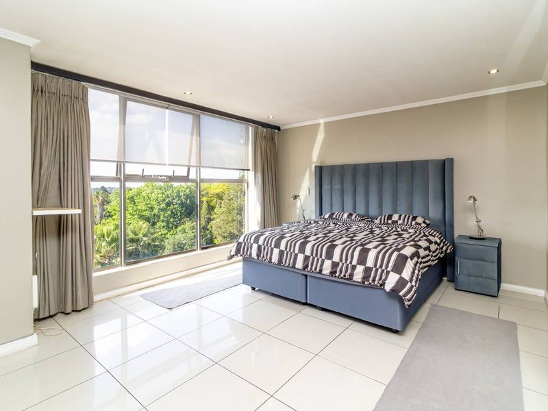 Spacious bedroom featuring large format floor tiles, recessed downlighting, and a expansive picture window offering pleasant green views.