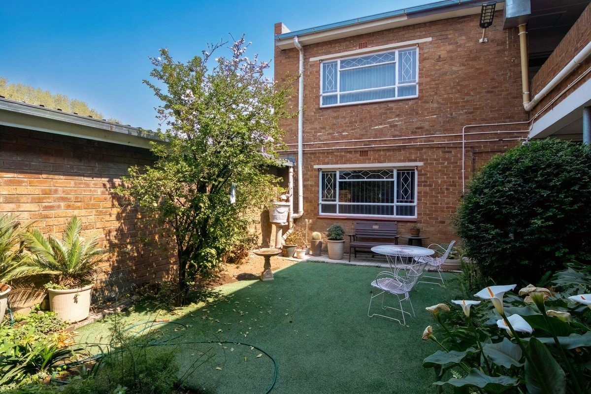 A private rear courtyard featuring a brick facade, artificial lawn, and established garden beds, providing a quiet outdoor space.
