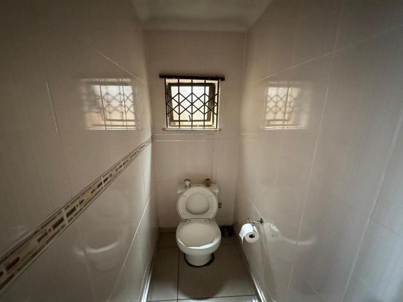 A compact, fully tiled guest toilet featuring a standard toilet suite and a small window with a security grille.