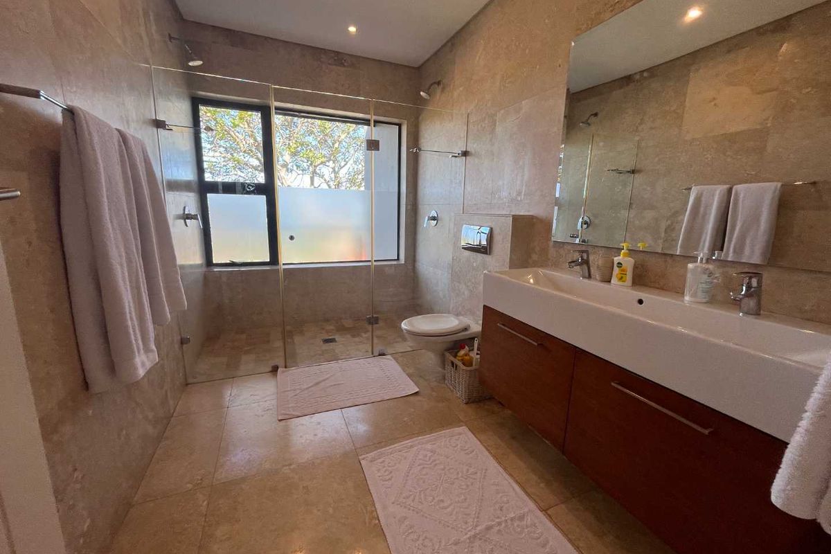 Modern bathroom featuring floor-to-ceiling stone tiling, a floating wooden vanity with a large basin, and a spacious walk-in glass shower enclosure.