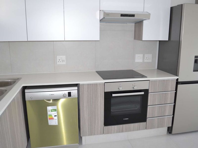 Modern kitchen featuring sleek white and wood-grain cabinetry, stone countertops, integrated dishwasher, and high-quality built-in appliances including an oven and electric hob.