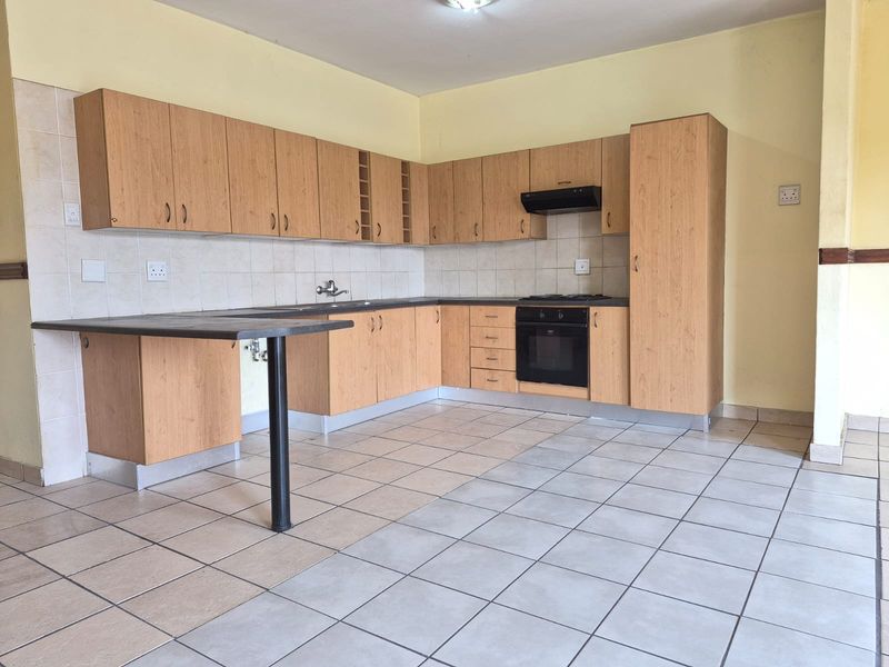 A functional kitchen featuring light wood-tone cabinetry, built-in oven and hob, tiled backsplash, and a breakfast bar extension.