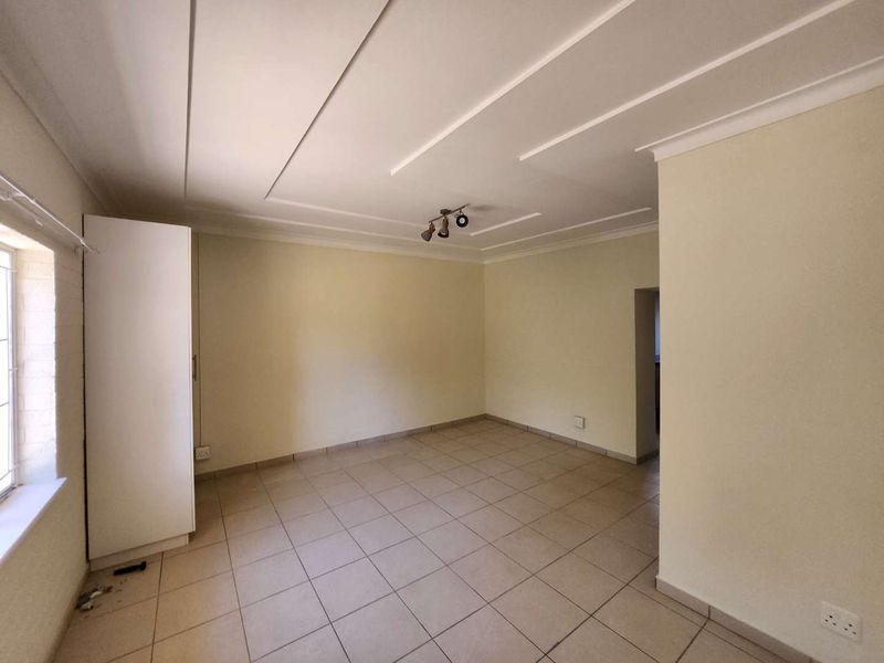 An empty living room featuring neutral tiled flooring, a built-in cupboard, and a coved ceiling with a central light fixture.