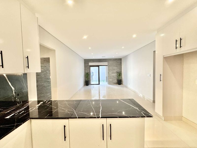 Modern open-plan living area featuring a sleek kitchen with black marble countertops, stone accent wall, and bright porcelain tiling throughout.