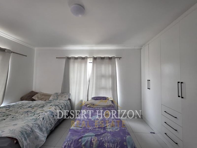A well-maintained bedroom featuring built-in cupboards, tiled flooring, and neutral wall finishes, providing a clean and functional living space.