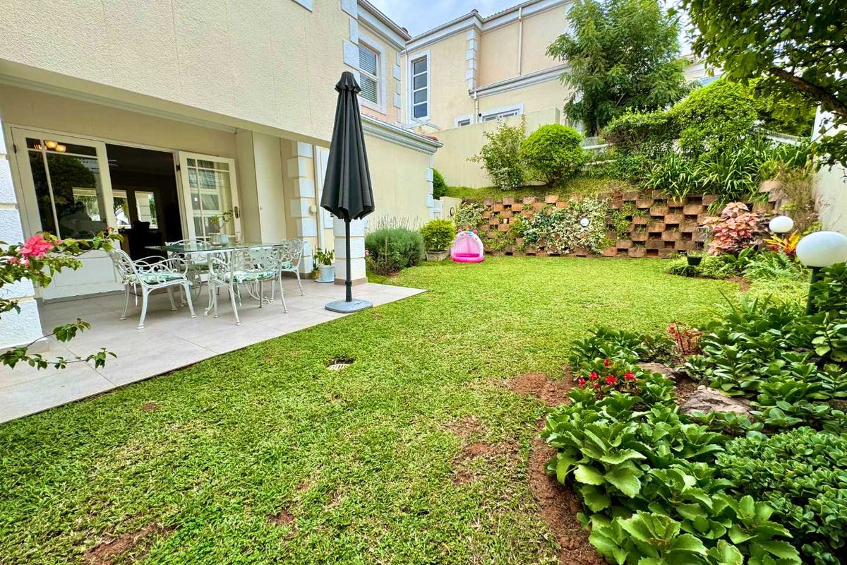 A private rear garden featuring a paved patio area, well-maintained lawn, and a tiered retaining wall with established garden beds.