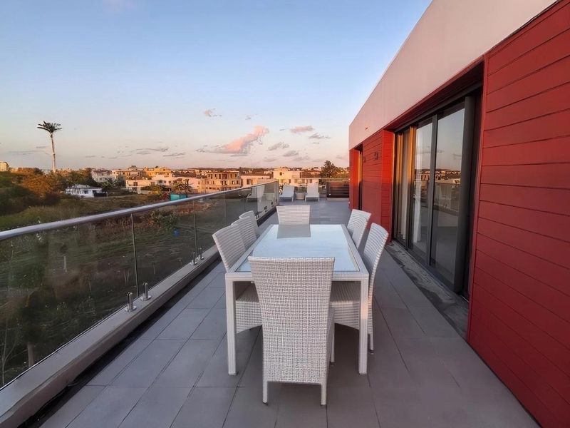 Spacious balcony featuring a modern glass balustrade, tiled flooring, and red exterior cladding, offering expansive views of the surrounding area.