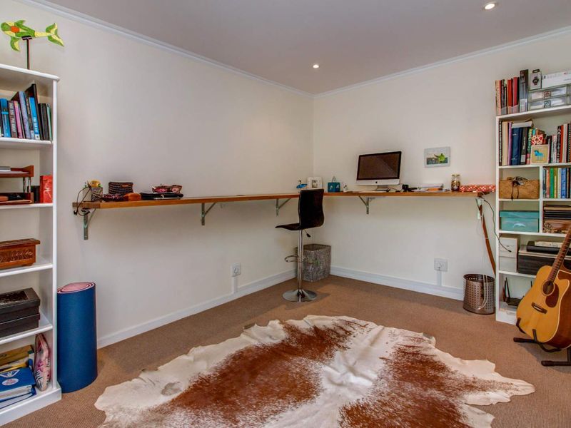 A functional home office space featuring a long, wall-mounted wooden desk and recessed ceiling lighting.